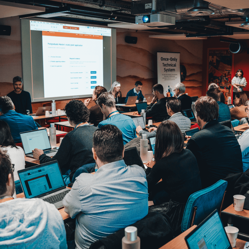 Participants attending the Once-Only Technical System Go-Live Accelerator event in Brussels, with the Common Services administration interface being presented on screen.